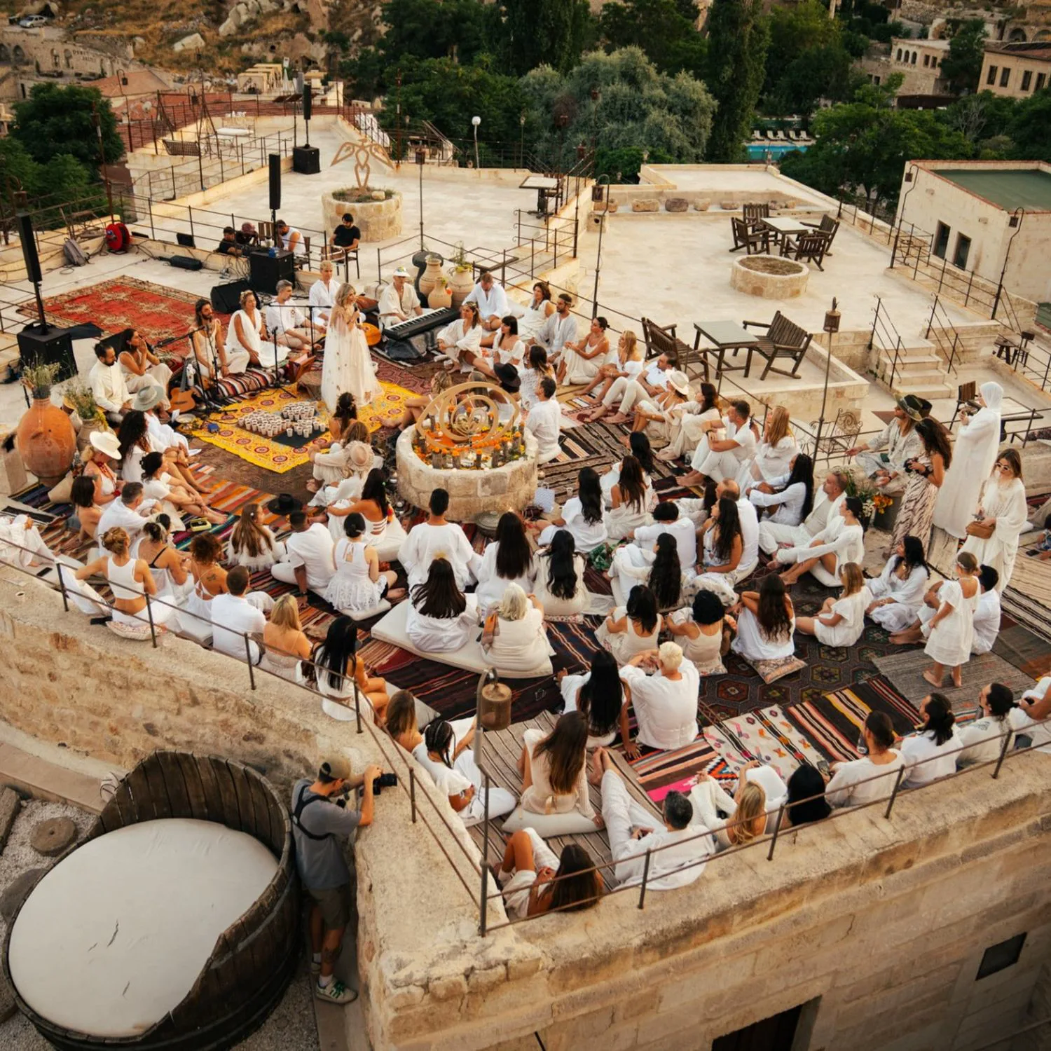 Participants dressed in white gathered on carpets on a Cappadocia rooftop for a music ceremony